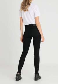 Pantalones vaqueros ajustados negros de tiro alto hechos de algodón elástico, con una textura suave y diseño tradicional de cinco bolsillos, combinados con botas negras hasta el tobillo.