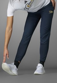 Laivaston siniset urheiluhousut, joissa on tyylikäs, istuva leikkaus ja vetoketjut nilkoissa. Yhdistetty valkoisiin lenkkitossuihin ja mustiin kuvioituihin sukkiin.