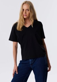 Zwarte V-hals t-shirt van zachte stof, met korte mouwen en een relaxte pasvorm. Draag het met blauwe denim jeans.
