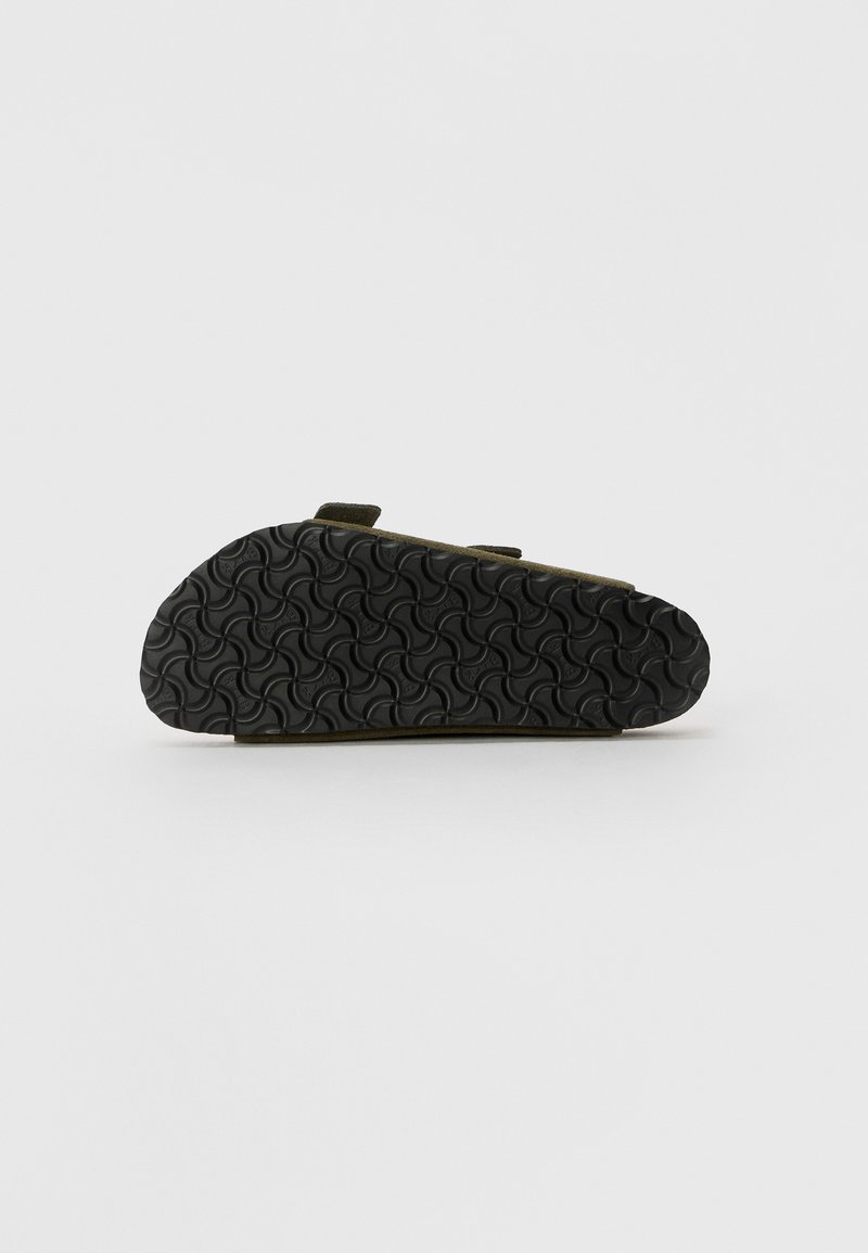 Semelle en caoutchouc noir avec un motif en ondulation ; partie supérieure vert olive avec deux sangles réglables pour un ajustement sécurisé. Design plat et décontracté.