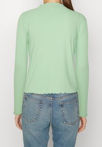 Dlouhý rukáv mintově zelený žebrovaný top se zvlněným lemem a manžetami, kombinovaný s vysokým pasem modrými džíny z denimu s nášivkovými kapsami.