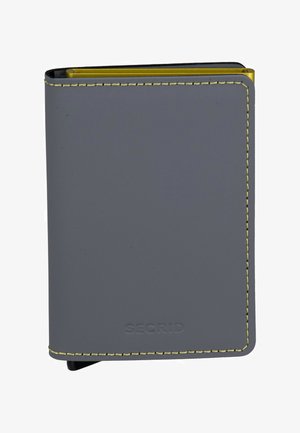 Cartera gris hecha de material suave con costuras amarillas. Presenta un diseño delgado con bordes redondeados y una marca en relieve en la parte inferior.