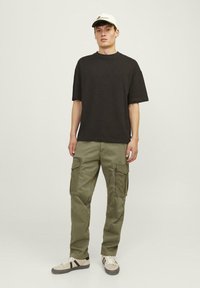 Zwarte oversized t-shirt gecombineerd met olijfgroene cargo-broek met meerdere zakken. Gekozen accessoires: een witte pet. Schoeisel: beige sneakers.