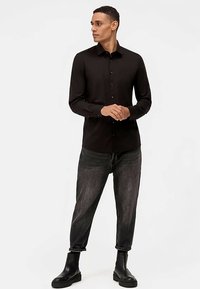 Camicia nera con bottoni in tessuto liscio, abbinata a jeans scuri. Il completo del modello è completato da stivaletti neri.