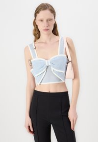 Crop top bleu et blanc à motifs avec un grand nœud, bretelles larges et bordure contrastante ; associé à un pantalon noir bien taillé.