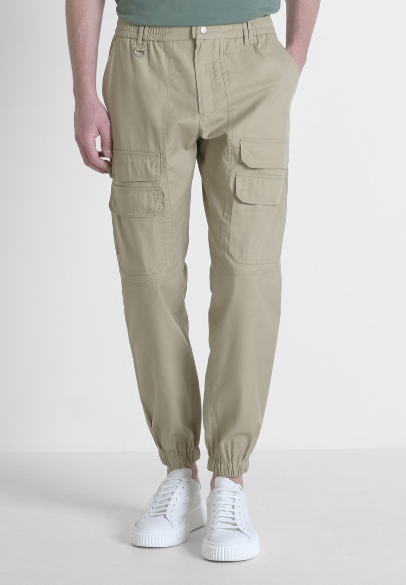 Beige cargobroek met elastische boorden en tailleband, met meerdere zijzakken en van een lichte stof, gecombineerd met witte sneakers.