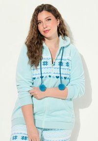 Sudadera con cremallera de forro polar azul claro con cordones de pom-pom, patrones de copos de nieve y triángulos, y puños acanalados. Textura suave y corte relajado.