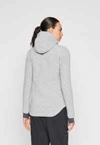 Haut en polaire gris avec capuche, manches longues et ouvertures pour les pouces aux poignets. Présente une texture lisse et un ourlet subtilement arrondi.