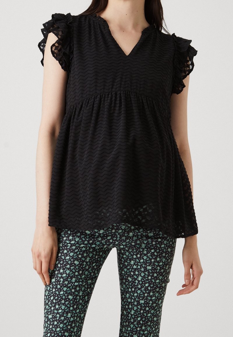 Blusa nera con scollatura a V, maniche a volant e motivo a zigzag testurizzato, abbinata a pantaloni neri con una piccola stampa floreale verde.