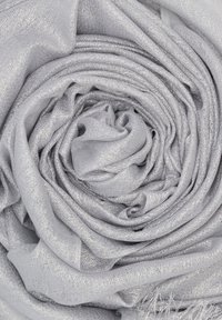 Scarf in tessuto metallico argento disposto a spirale. Morbido al tatto con una leggera lucentezza e bordi frangiati. Design leggero e fluido.