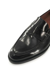 Zwarte leren instapper met een gladde afwerking, puntige neus en decoratieve stiksels over de wreef. Platte zool en minimale hardware-details.