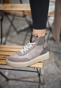 Baskets grises avec lacets blancs, en matériaux en daim et en cuir, design montante, semelle texturée et accent logo doré.