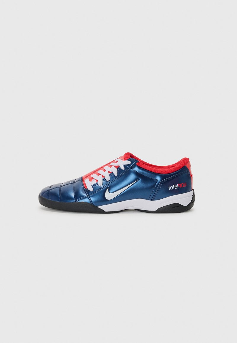 Nike Total90 soccer shoe with a blue synthetic upper, red accents, white laces, textured design, and black rubber sole.