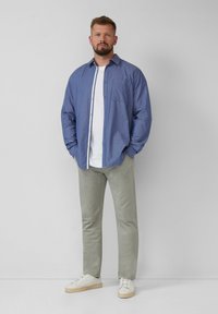 Codzienny zestaw ubrań z niebieską koszulą w wzory, białą koszulką, jasnoszarymi spodniami i białymi trampkami. Koszula ma guzikowe zapięcie.