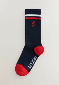 Marine crew sok met een rood-wit gestreepte rand, rode teen en witte tekst met de woorden "SUPERDRY" op de onderkant. Gebreide structuur.