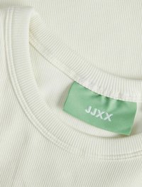 Cremefarvet ribbet bomulds t-shirt med rund halsudskæring. Funktioner et grønt stofmærke med "JJXX" i hvid syning. Glat tekstur.