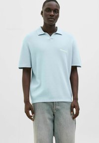 Lyseblå kortærmet polo med en afslappet pasform, der har krave og diskret mærke-broderi på brystet. Bæres med lyse denim jeans.