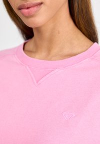 Roze sweatshirt met een ronde hals, geribbelde manchetten en een klein hartlogo geborduurd op de borst. Zachte stof met een gladde textuur.