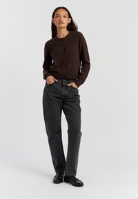 Bruine gebreide cardigan met ronde hals en knoopsluiting, gecombineerd met hoge zwarte spijkerbroek en zwarte loafers.