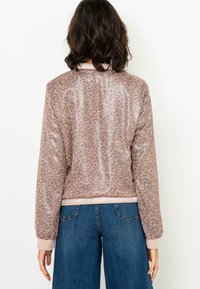 Floral bomber jacket in light brown with pink flowers, shiny texture, ribbed cuffs, and hem; paired with wide-leg blue jeans.