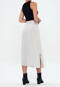 Jupe midi blanche avec une fente, présentant un motif de petits points noirs dispersés. Associée à des bottines noires et à un crop top noir ajusté.