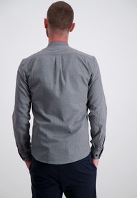 Harmaan pitkähihaisen paidan, jossa on teksturoitu kuvio, kauluksessa nauha ja takana laskos. Varustettu napillisilla hihansuilla ja huvittavalla istuvuudella.