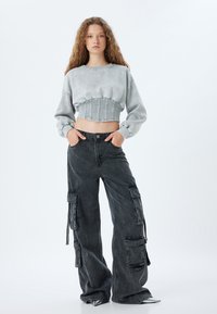 Sudadera gris recortada con una banda elástica texturizada y acanalada, combinada con pantalones cargo negros de corte holgado que presentan múltiples bolsillos.