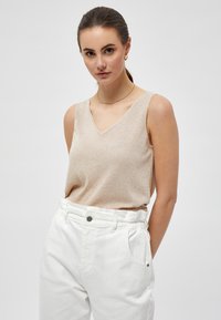 Beige v-neck sleeveless top made of a soft, textured fabric, paired with high-waisted white pants featuring a button and side pockets.