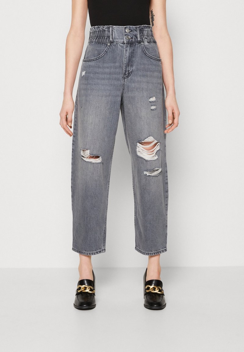 Jeans grises de tiro alto y rotos con una cintura elástica, que presentan varias zonas desgastadas y un corte relajado. Combinados con mocasines negros.