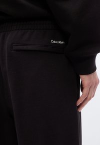 Μαύρο φανελένιο παντελόνι με απαλό υφή, διαθέτοντας πλαϊνή τσέπη με οριζόντια είσοδο και μικρό λευκό λογότυπο "Calvin Klein".