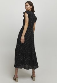 Svart maxiklänning med vit blommig tryck, texturerad bodice, volangärmar och lagerkjol. Bärs med ljusgrå blockklackssandaler.