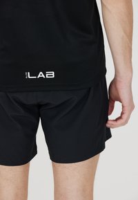 Musta urheilu paita, jossa on verkotettu pinta ja "elite LAB" -logo. Yhdistetty mustiin shortseihin, jotka korostavat virtaviivaista muotoilua ja kevyttä materiaalia.