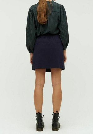 Blusa a strisce verde scuro con maniche a palloncino abbinata a una gonna blu navy. La modella indossa stivali neri alla caviglia. Sfondo semplice.
