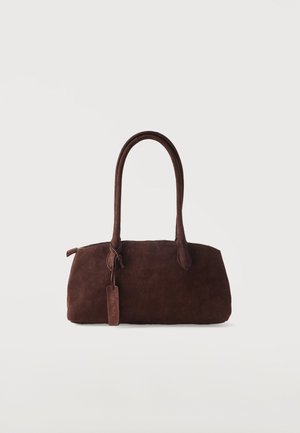 Sac à main en daim marron foncé avec deux longues anses et une petite étiquette attachée, sur un fond clair uni.