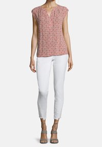 Blusa color salmone con un motivo geometrico, maniche a sbuffo e scollatura a V. Abbinata a jeans bianchi slim fit e sandali grigi con cinturini.