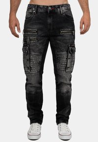 Black denim jeans with a slim fit, featuring multiple zippered pockets, ribbed detailing on the knee area, and red stitching accents.