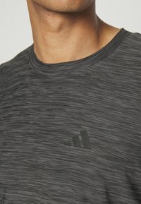 Camiseta atlética de mezcla negra con cuello redondo y mangas cortas. Presenta una tela sutil y texturizada, y un logo en la esquina inferior izquierda.