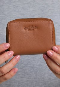 Brown leather zip wallet with a smooth texture, rectangular shape, embossed logo on the front, and metal zipper detail along the edge.