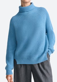 Pulover tricotat de culoare albastru deschis cu guler înalt, textură ribbed și umeri coboară, asortat cu pantaloni din țesătură gri.