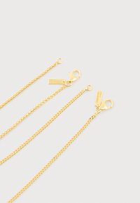 Τρεις χρυσές αλυσίδες με κούμπωμα αστακού και μικρές ορθογώνιες πλακέτες χαραγμένες με τη λέξη "COMMONLINES" σε ανοιχτό φόντο.