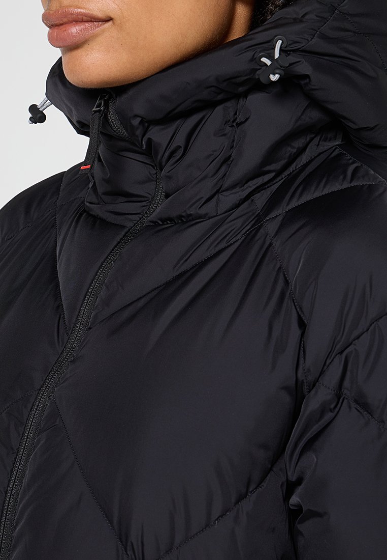 Nahaufnahme einer Person, die eine schwarze, gesteppte Daunenjacke mit hohem Kragen und verstellbaren Kapuzenbändern trägt.