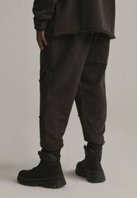 Czarne, zwężane dresy o miękkiej fakturze i elastycznych mankietach. Noszone z czarnymi, masywnymi butami na sznurówki. Posiadają boczne kieszenie.