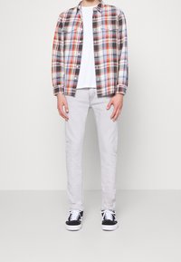 Camicia di flanella a quadri rossa, blu e nera; t-shirt a collo rotondo bianca; jeans grigi chiari; sneakers bianche e nere.