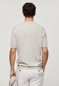 Pull à manches courtes gris clair en maille avec un col rond et un ourlet côtelé, porté avec un pantalon de couleur claire. Texture lisse, détails minimaux.