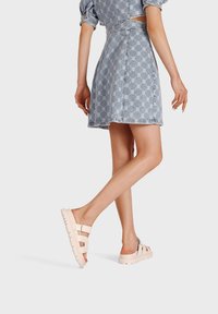 Sandali piattaforma beige con due fasce larghe, suola testurizzata e retro aperto. Indossati con un vestito di jeans caratterizzato da un design a fantasia.