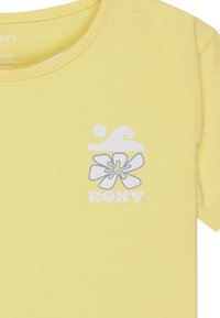 T-shirt en coton jaune avec un graphique représentant des vagues blanches et des fleurs, avec le texte "ROXY" en dessous. Manches courtes et encolure ras du cou.