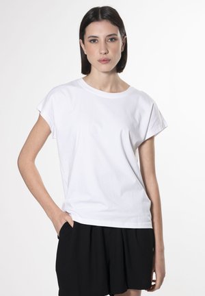White, short-sleeve t-shirt with a round neckline, made of cotton fabric. Paired with black shorts, featuring a relaxed fit and smooth texture.