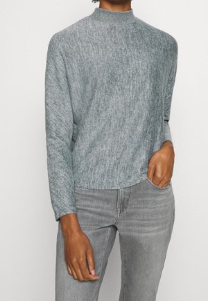 Lichtgrijze gemarmerde gebreide trui met een hoge halslijn en lange mouwen, gestyled met lichtgrijze jeans; zachte textuur en ontspannen pasvorm.
