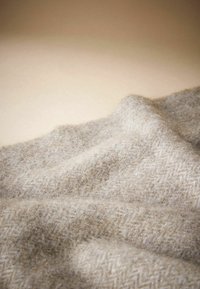 Mīksts beigstēvs vilnas audums ar teksturētu Herringbone rakstu, izkārtots tā, lai parādītu viļņus un krokas, izceļot tā siltumu un komfortu.