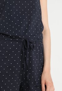 Combinaison bleu marine ornée de petits pois blancs, taille élastique à cordon, et tissu léger à texture lisse.